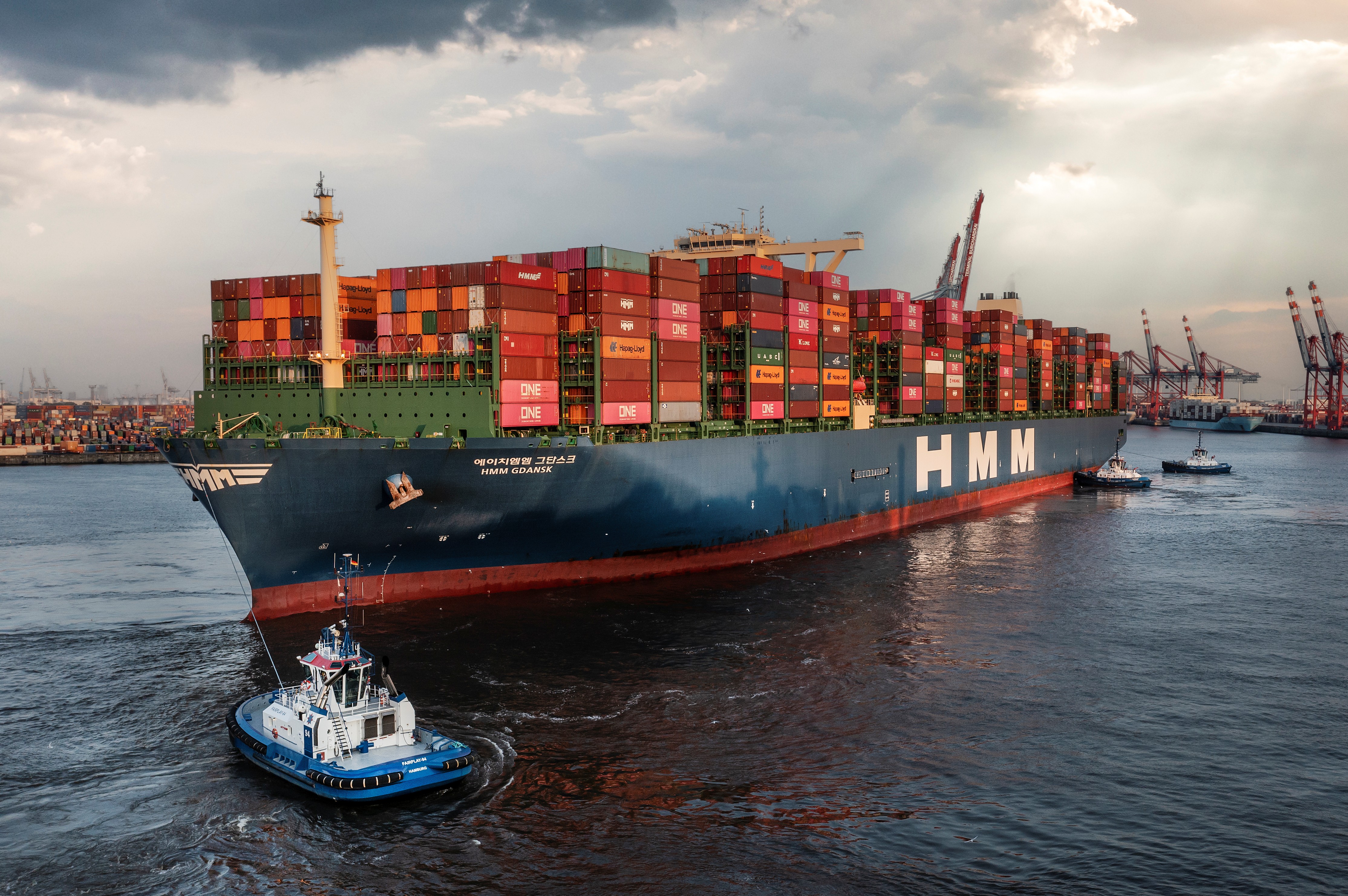 Großes, beladenes Containerschiff hinter einem kleinen Schlepperboot