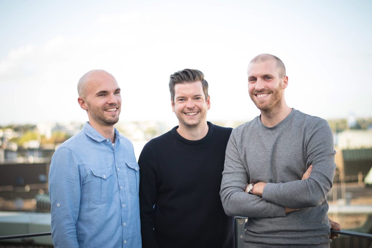 Drei junge, innovative Gründer, die freundlich und motiviert in die Kamera blicken.