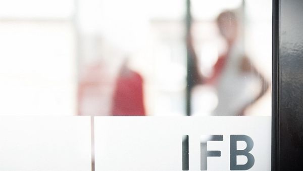 IFB Logo auf Milchglas, im Hintergrund ist eine Person zu sehen.