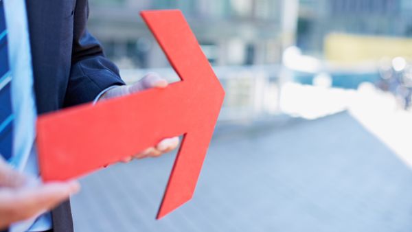 Mann im Anzug hält einen roten nach links gerichteten Pfeil in der Hand