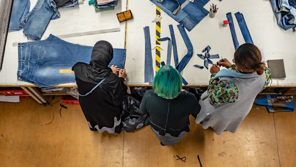 Drei Frauen bearbeiten Stoffe an einem Tisch
