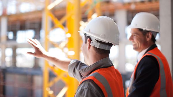 Zwei Herren, die sich vor einer Neubau-Baustelle unterhalten und dabei gestikulieren.