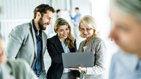 Drei Personen beugen sich über einen Laptop und lächeln