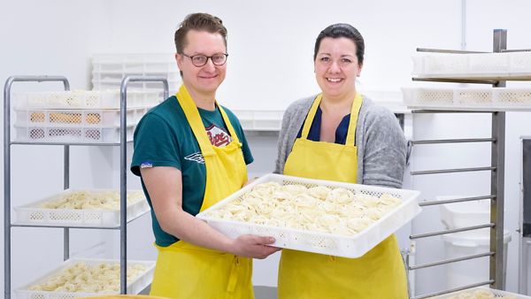 Eine Dame und ein Herr präsentieren Ihre selbstgemachte Pasta, die Sie im Rahmen einer Gründung herstellen.
